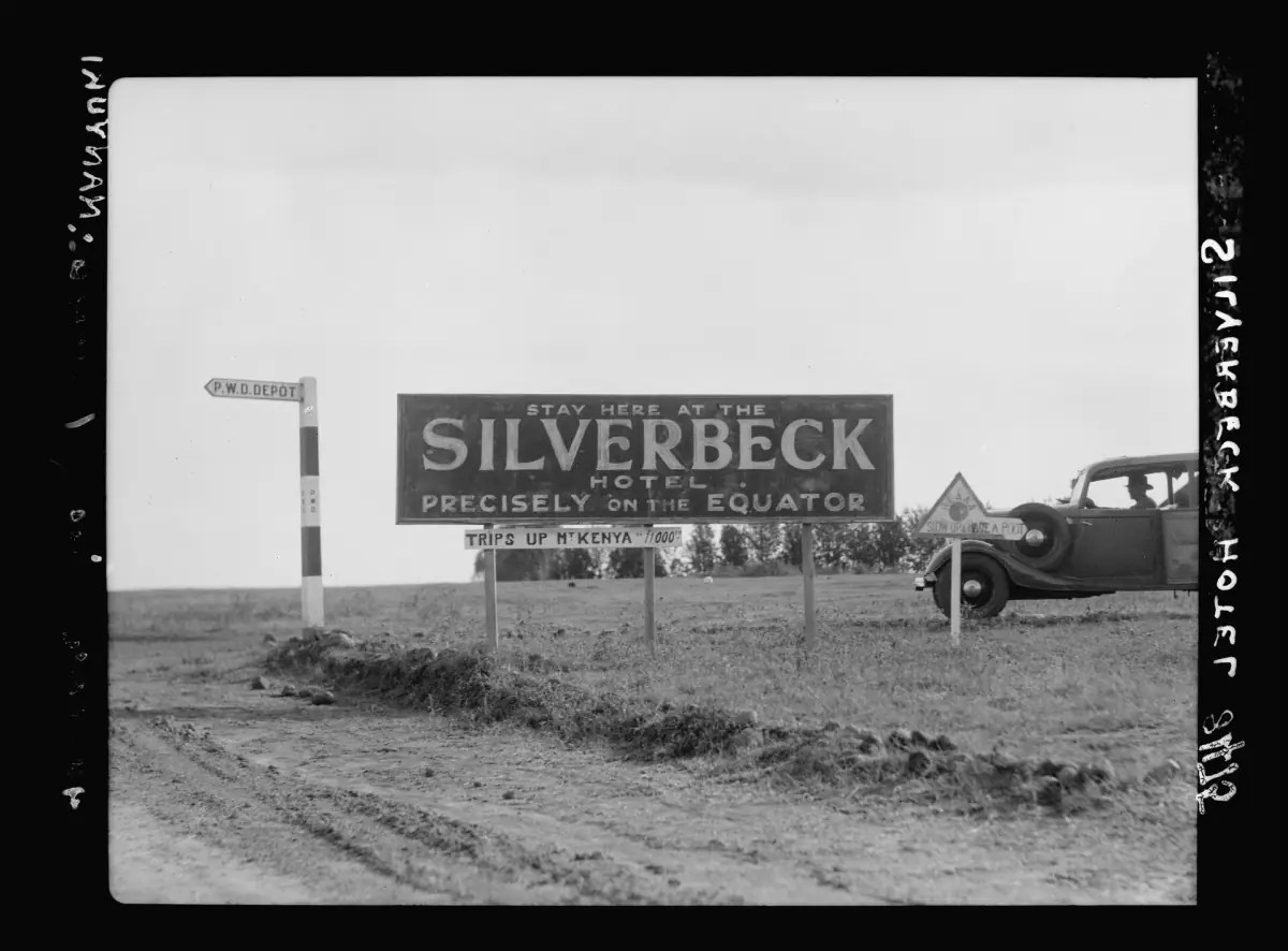 Black and white photo of a signboard on the equator beside a dirt road